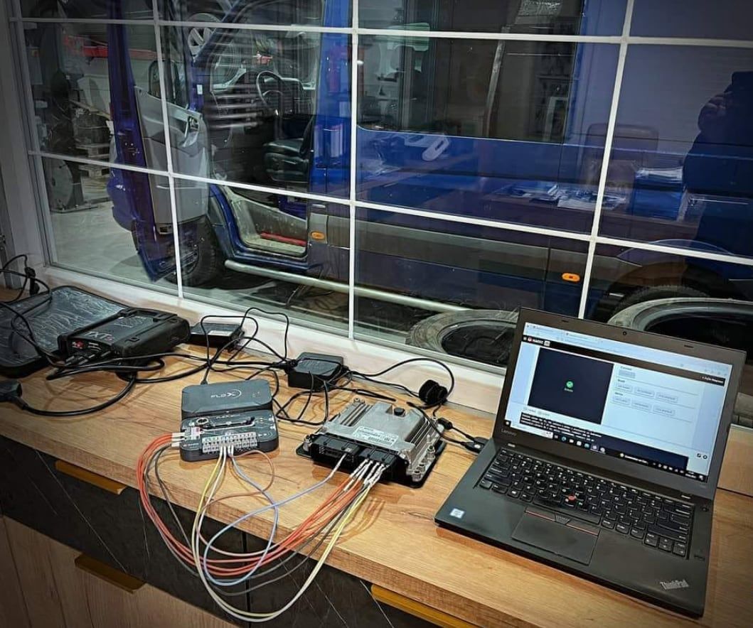 Sterownik silnika podłączony przewodami do programatora i laptopa na stole warsztatowym